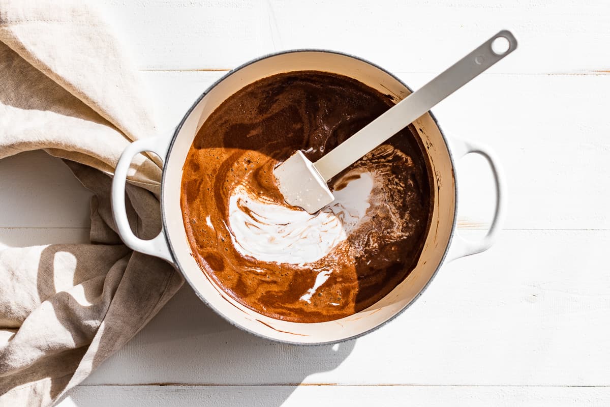 Adding the milk to the cocoa powder mixture in a white pot.