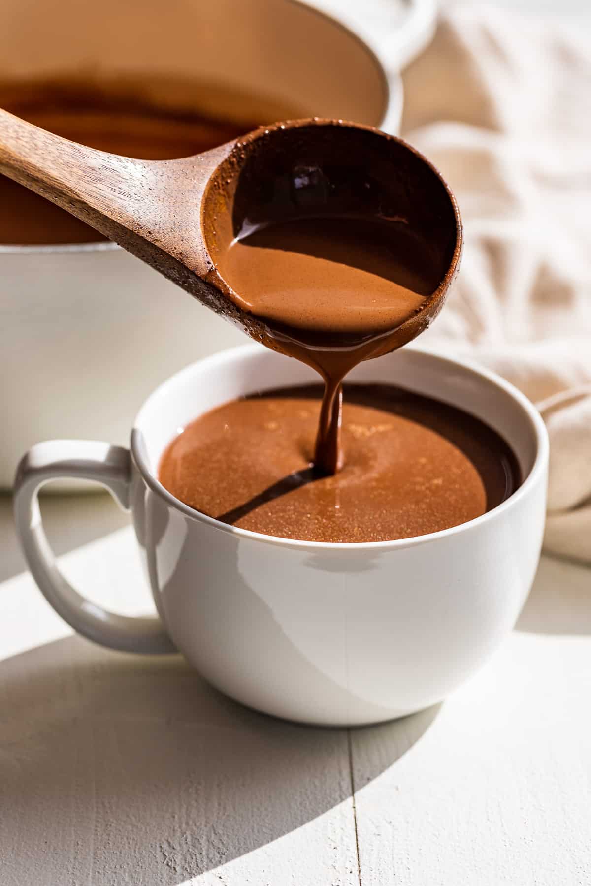 Wooden ladle pouring hot chocolate into a large white mug.