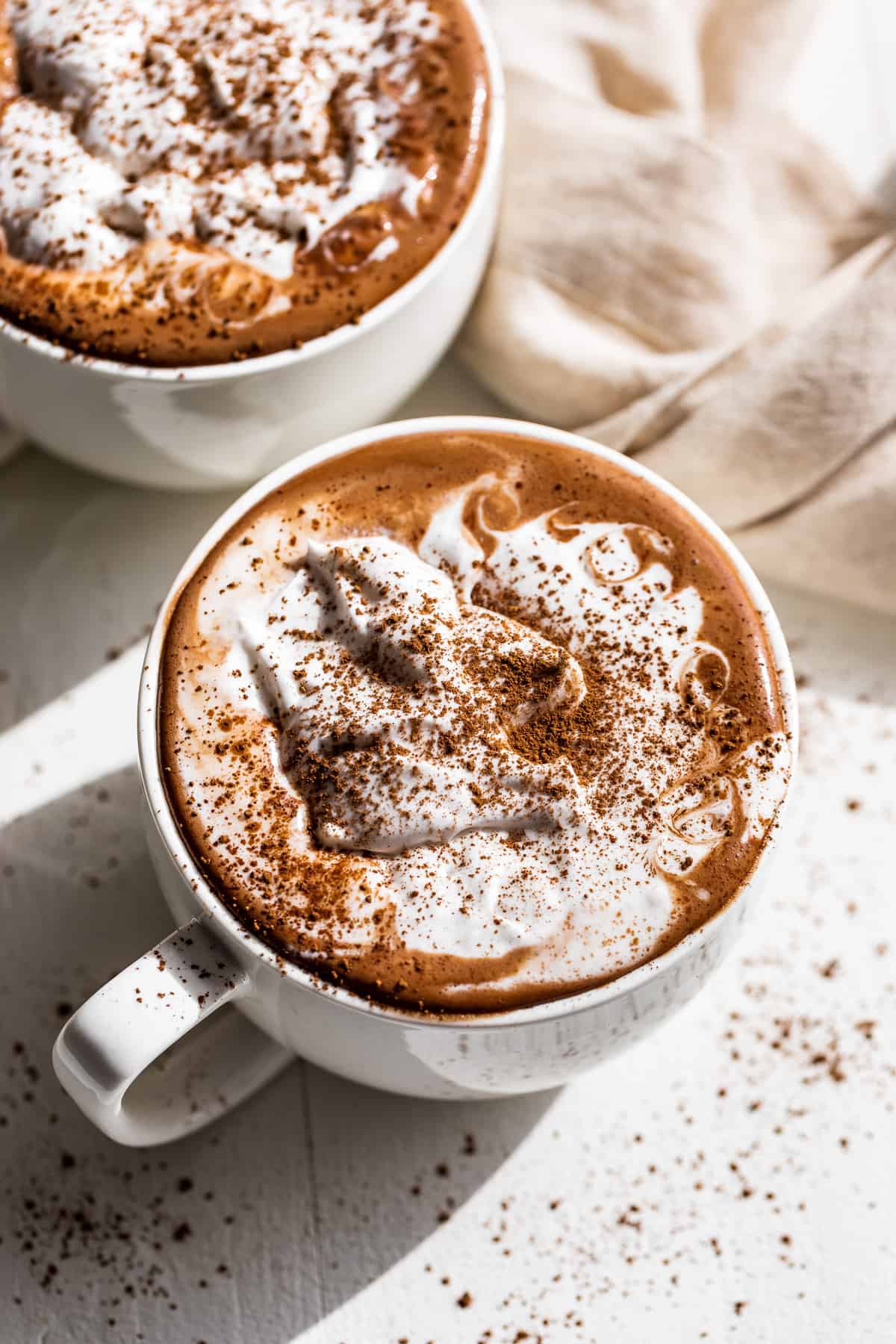 Downward view of two mugs of hot chocolate topped with whipped cream.