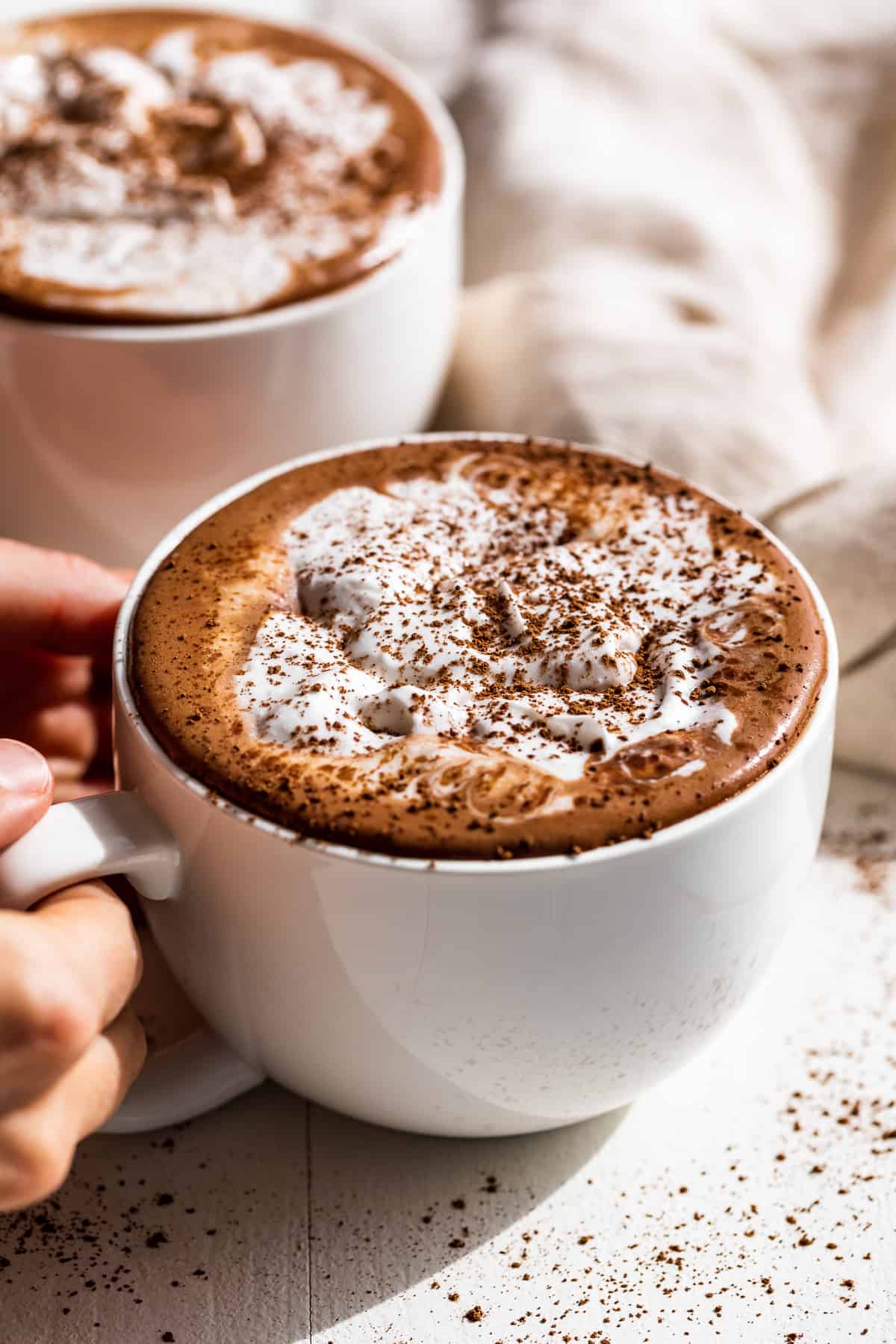 Hands holding a large white mug of hot chocolate topped with whipped cream.
