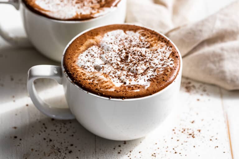 Two large mugs of Homemade Hot Chocolate topped with whipped cream and cocoa powder.