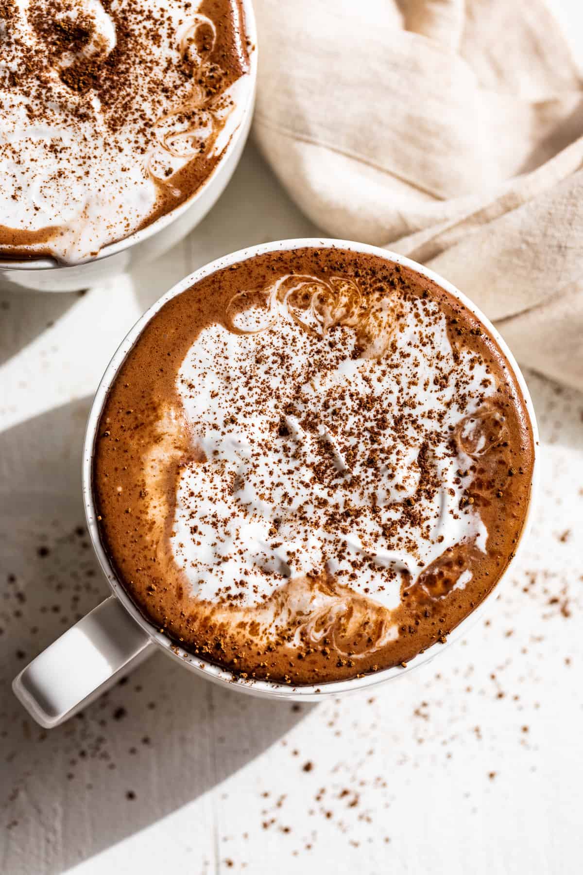 Straight down view of two mugs of hot chocolate topped with whipped cream.