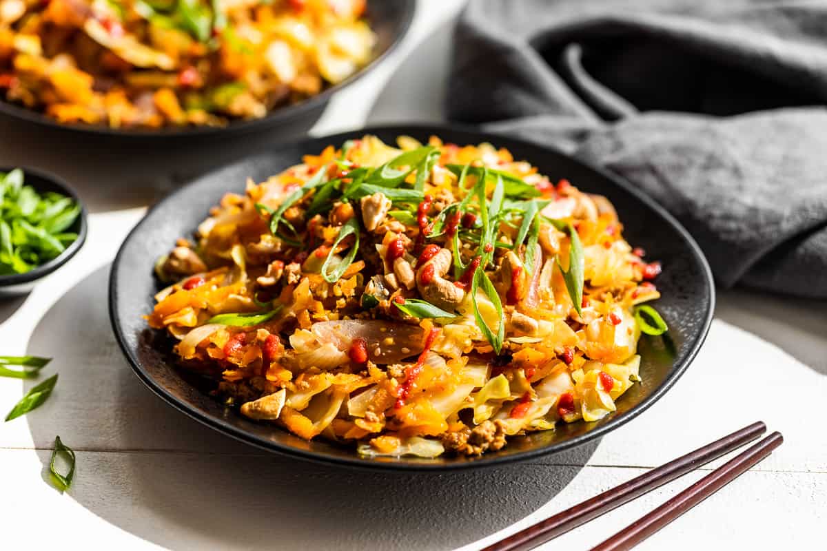 2 black plates of finished Egg Roll Bowl topped with green onions and cashews.