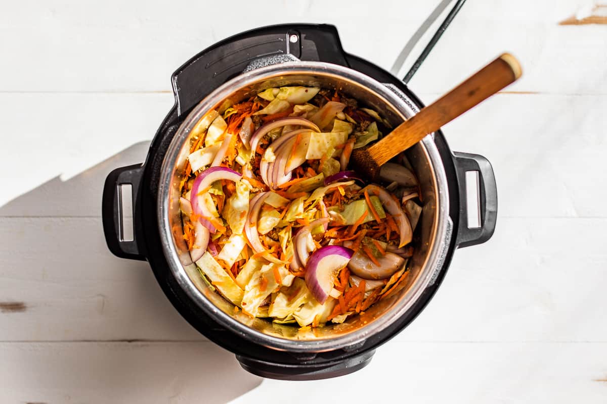 Cabbage, carrots, and onions being added to the instant pot.