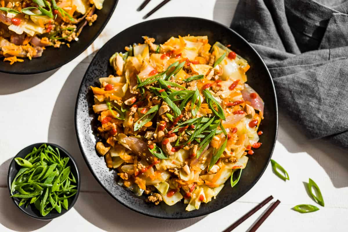 Straight down shot of Egg Roll Bowl piled onto 2 black plates with green onions on the side.