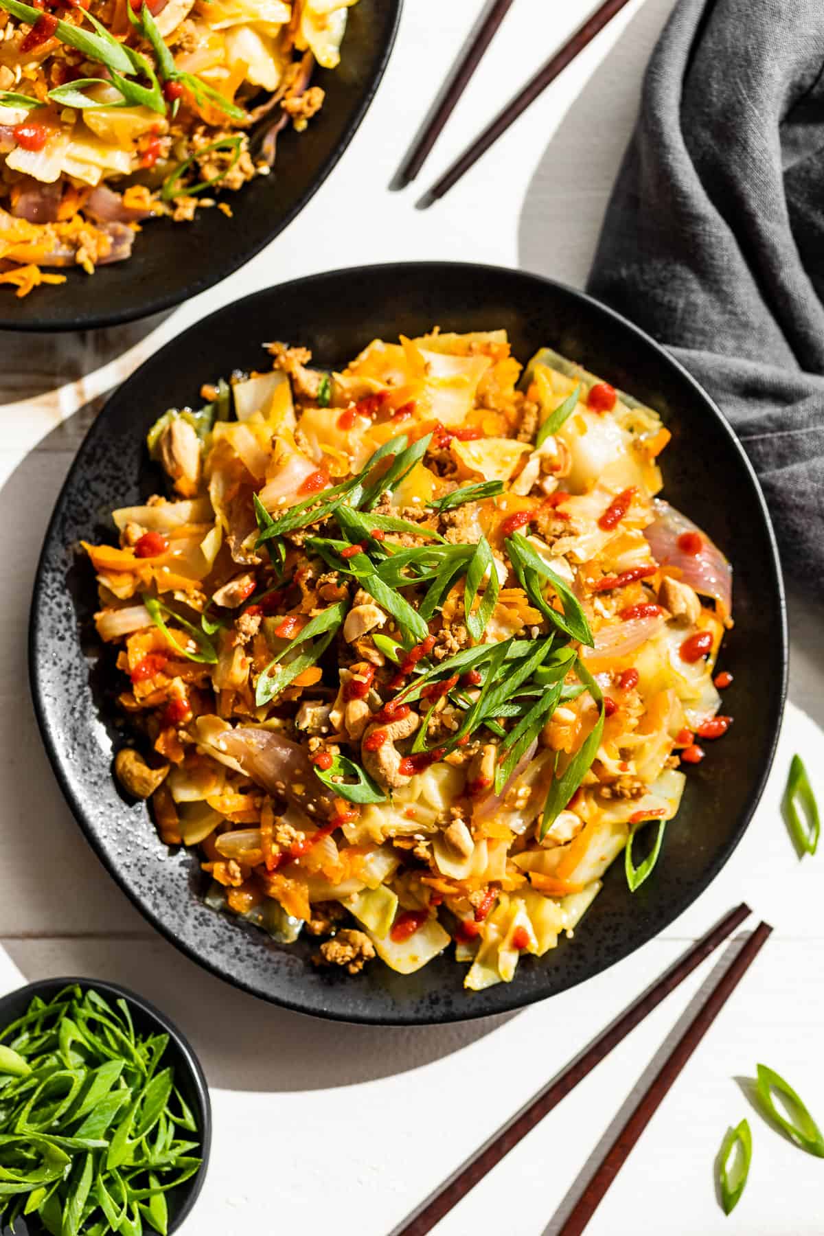 Two black plates piled with egg roll bowl and topped with green onions and sriracha.
