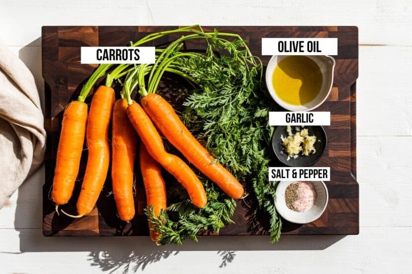 Carrots, olive oil, garlic, sea salt, and pepper on a wooden cutting board.