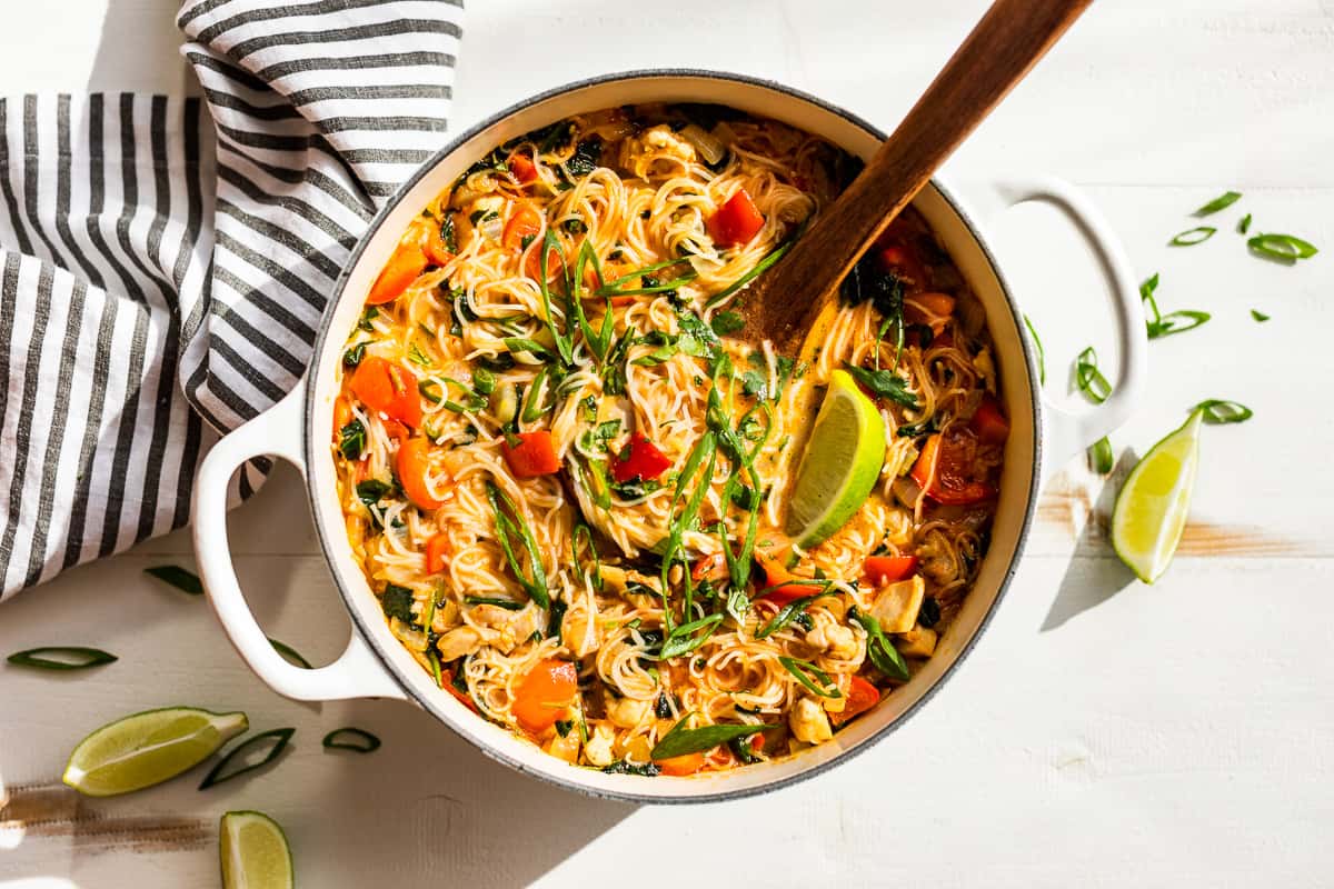 Finished Thai Curry Noodle Soup with a wooden ladle on a white background.