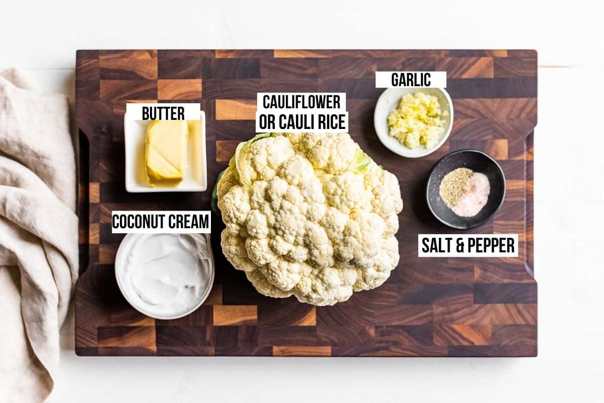 Cauliflower, coconut cream, butter, garlic, salt & pepper on a wooden cutting board.
