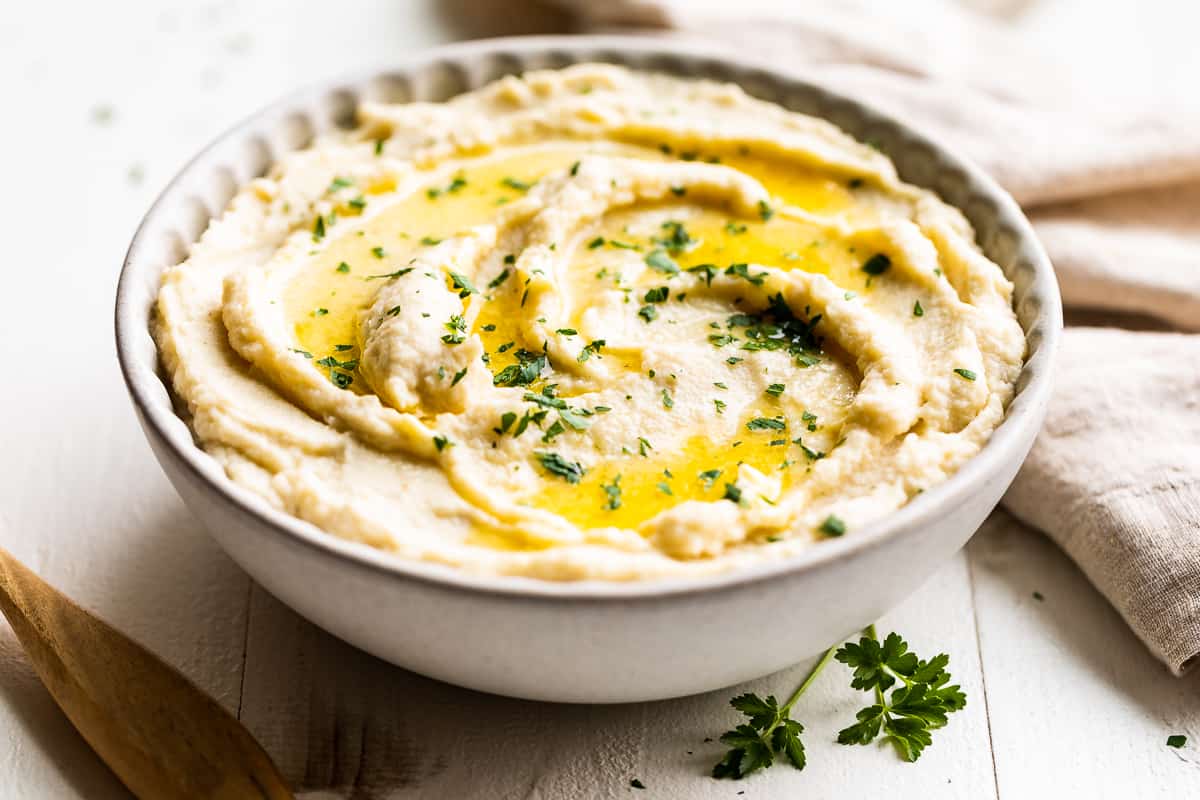 Creamy Mashed Cauliflower in a pottery bowl with a wooden spoon.