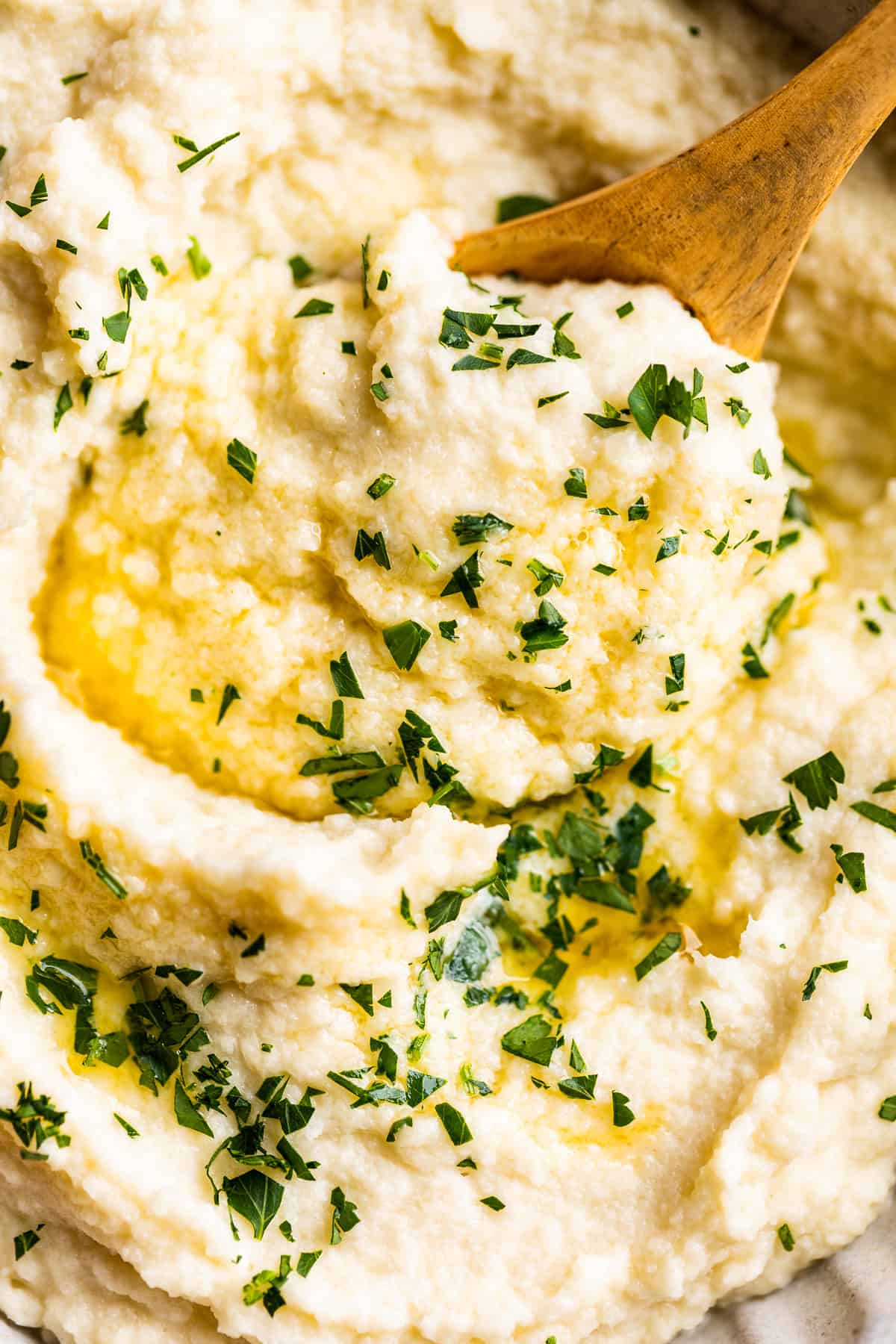 Close up view of mashed cauliflower topped with butter and parsley.