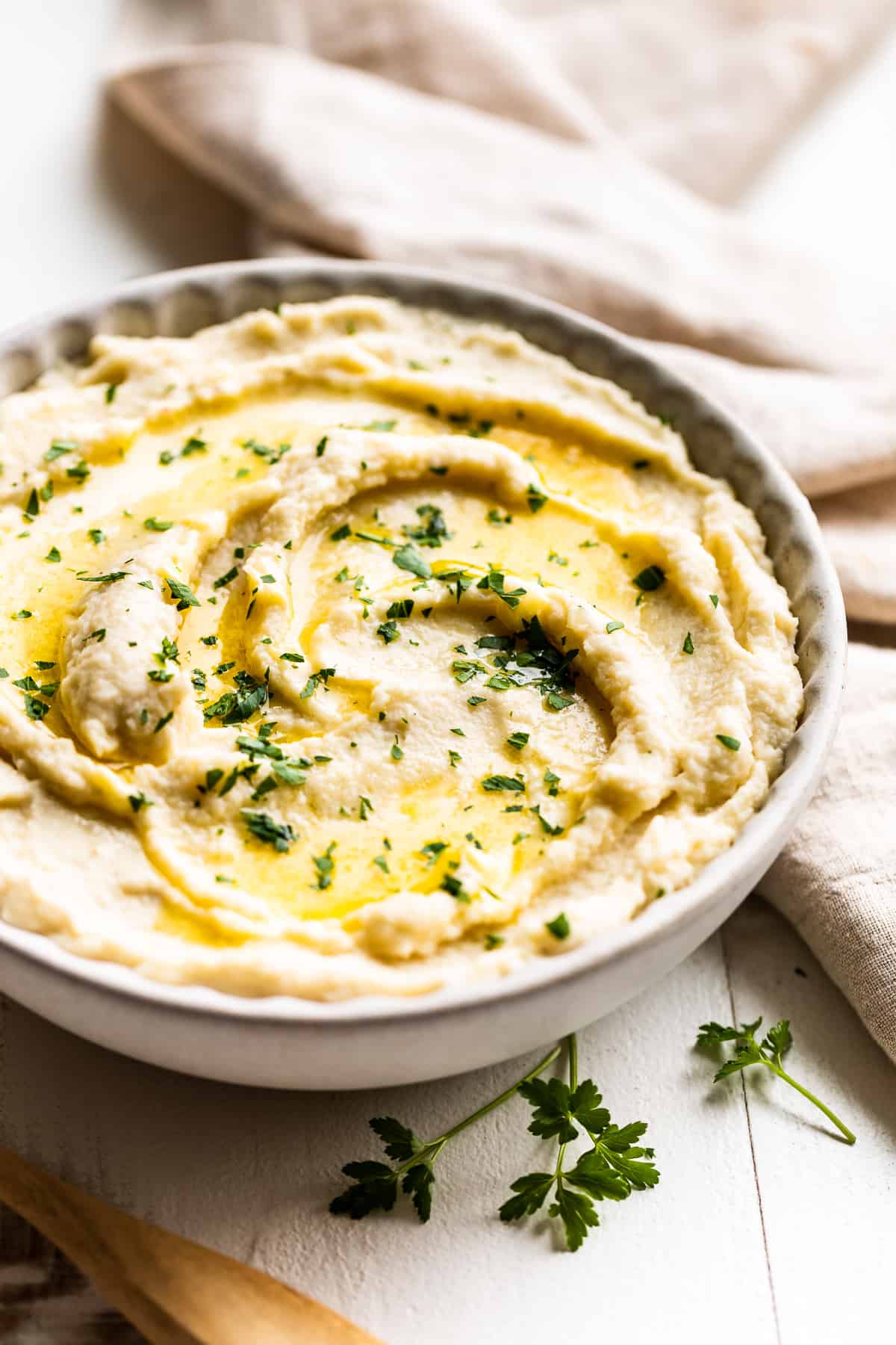 Grey bowl filled with mashed cauliflower and a wooden spoon.