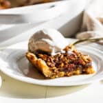 A pecan pie bar on a white plate with a scoop of vanilla ice cream on top.
