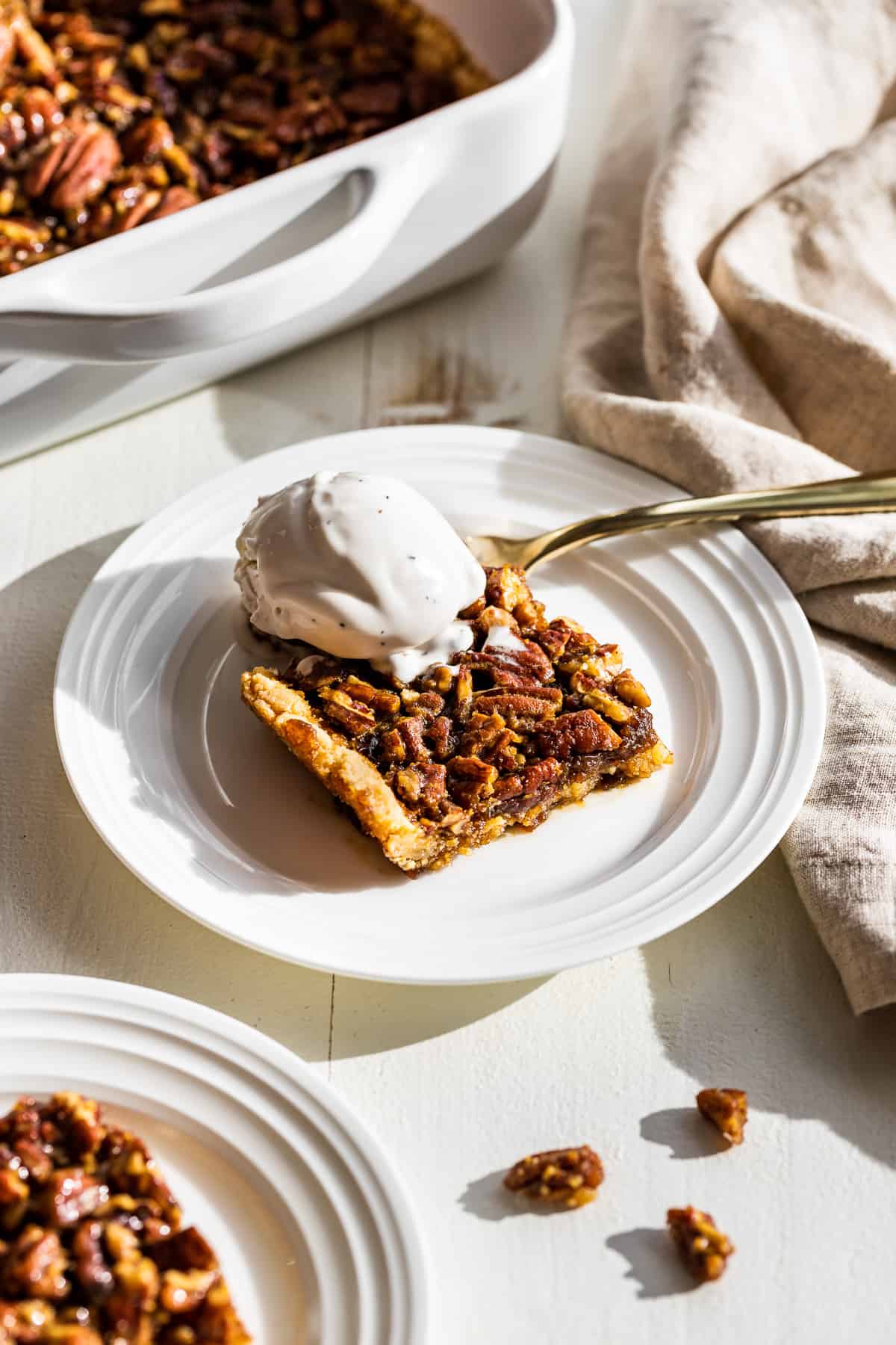 Side view of two plates of pecan pie bars with a scoop of vanilla ice cream on top.