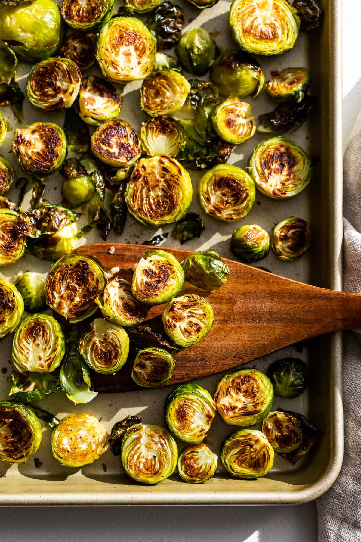 Sheet pan of roasted Brussels Sprouts with a wooden spatula.