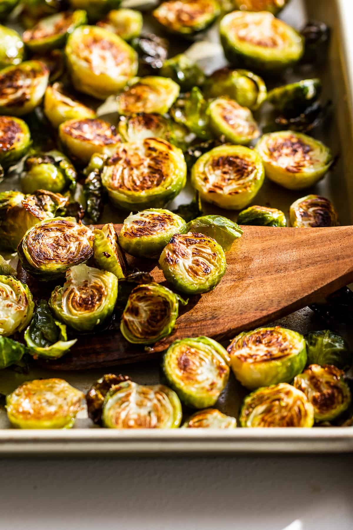Side view of Roasted Brussels Sprouts with a wooden spatula scooping some out.