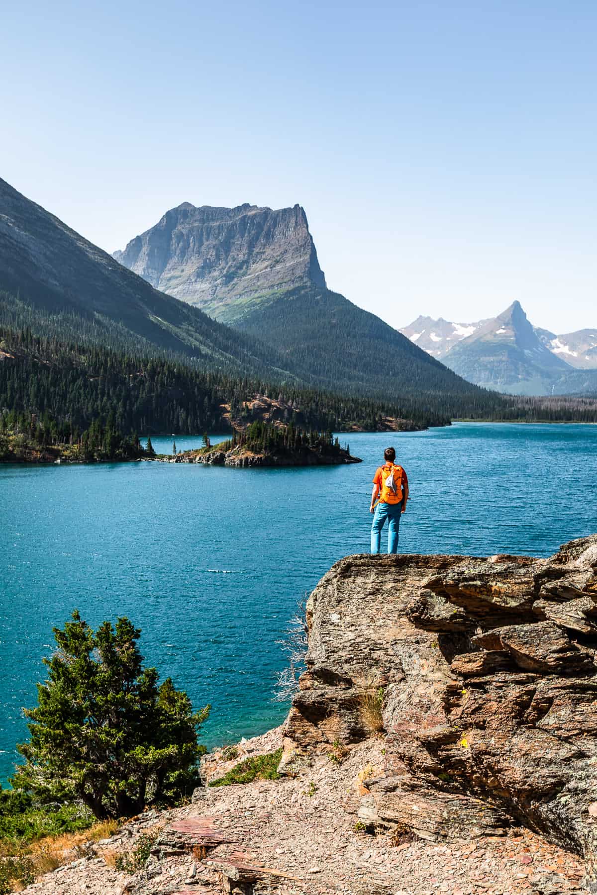 Man with an orange backpack looking out over St. Mary Lake in Glacier National Park.