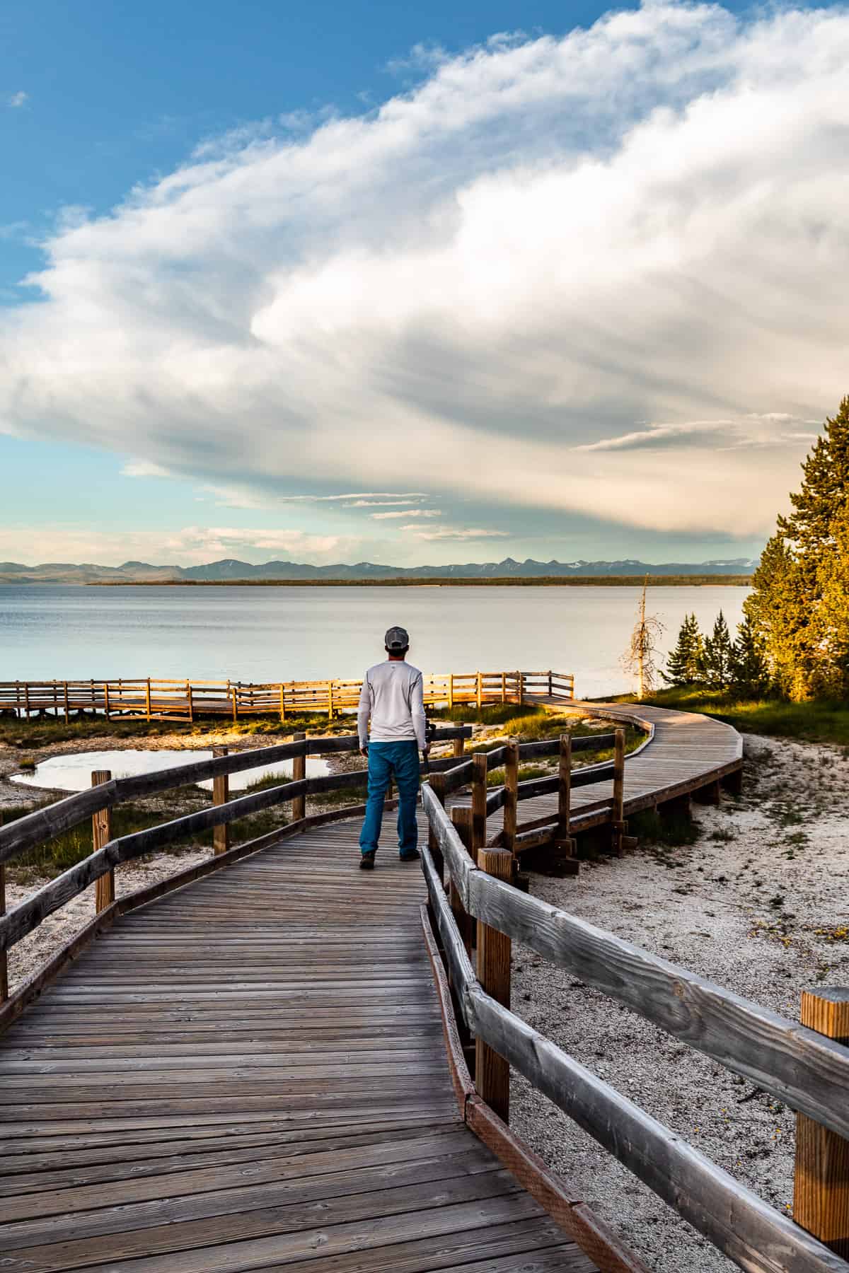 A man walking down the boardwalk in the West Thumb Geyser Basin overlooking Yellowstone Lake at sunset.