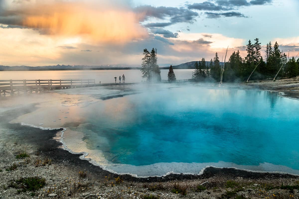 Overlooking a bright blue geyser on the edge of Yellowstone Lake at sunset.