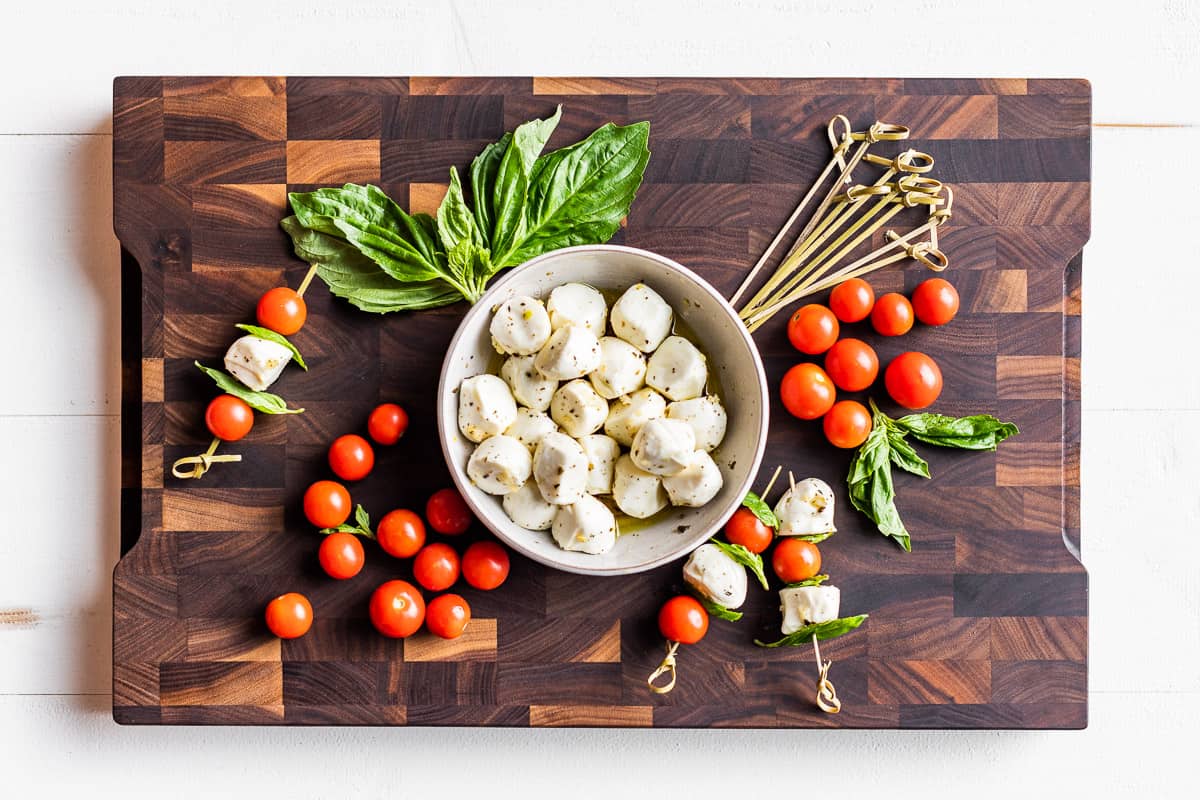 Marinated mozzarella, cherry tomatoes, basil, and skewers on a wooden cutting board.