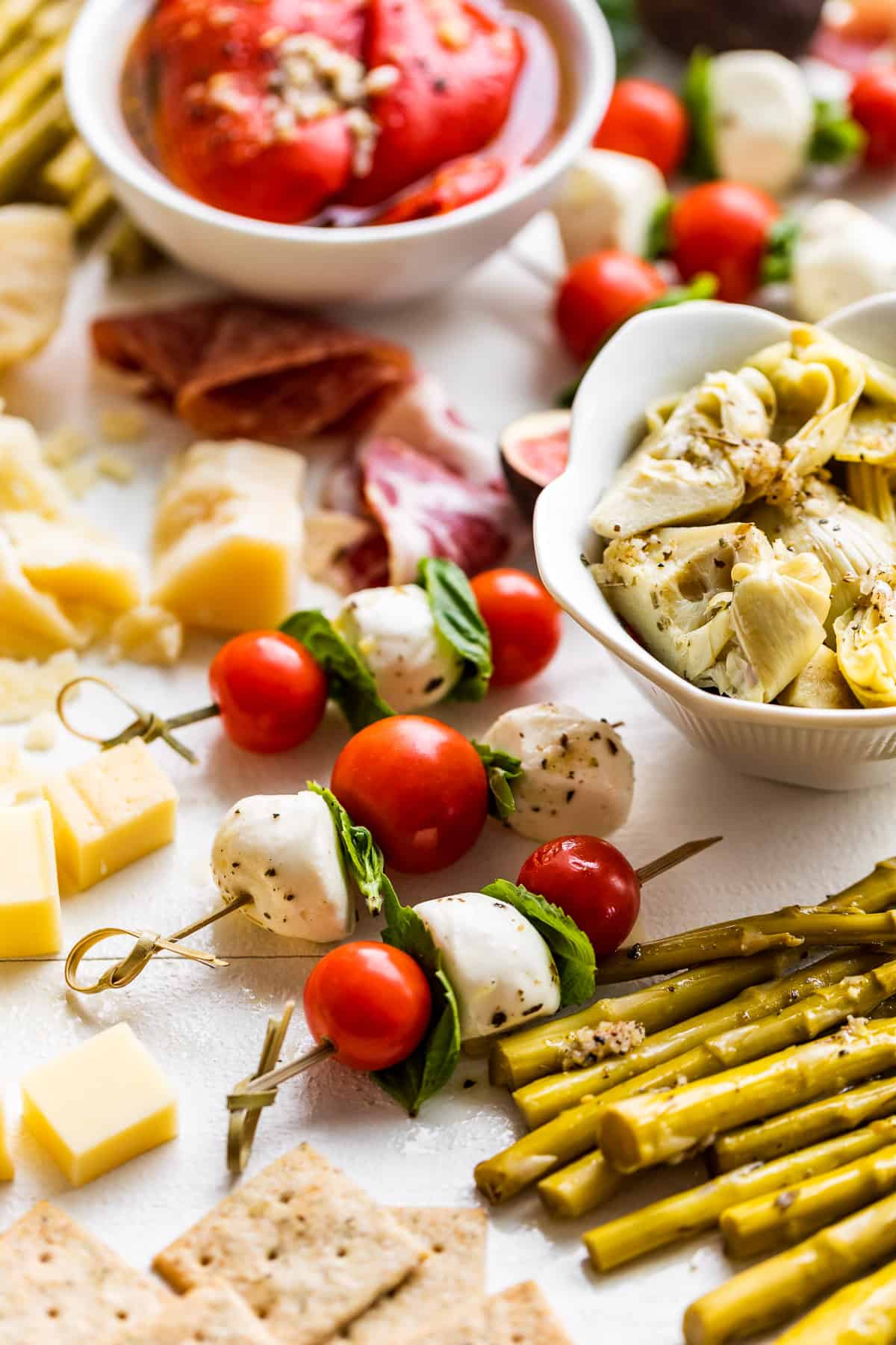 Close view of marinated peppers, asparagus, and artichokes with cheese cubes around the bowls.