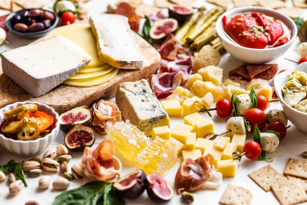 All the ingredients for the Antipasto Platter on a large white board. Marinated veggies, caprese skeweres, figs, cheeses, and sliced salami.