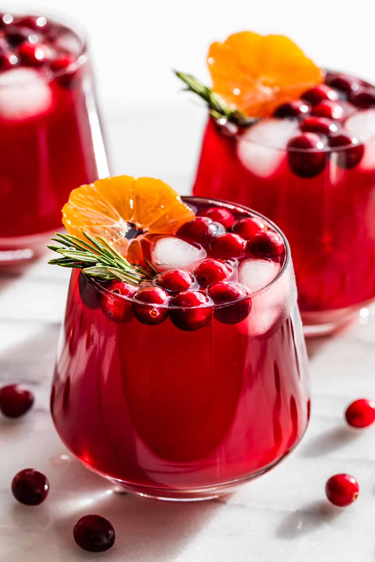 Three glasses of Cranberry Kombucha Mocktails topped with orange slices, cranberries and rosemary sprigs.