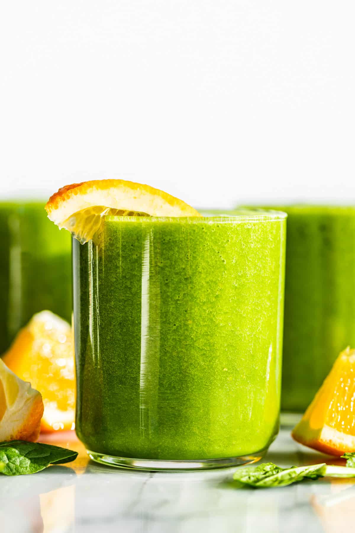Three glasses Detox Green Smoothie with orange wedges on top and around the glasses.