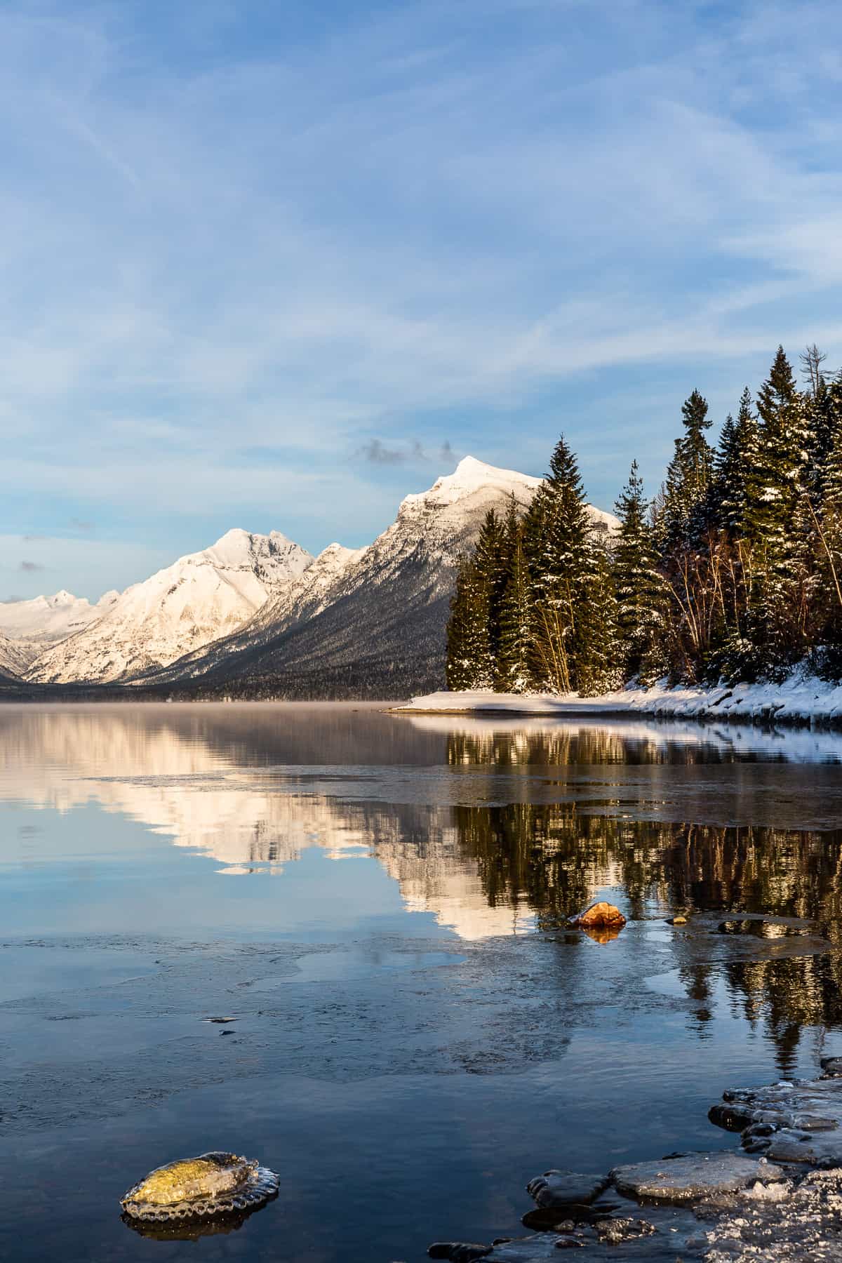 Snowy mountains reflecting into a lake with trees and snow on the shoreline.