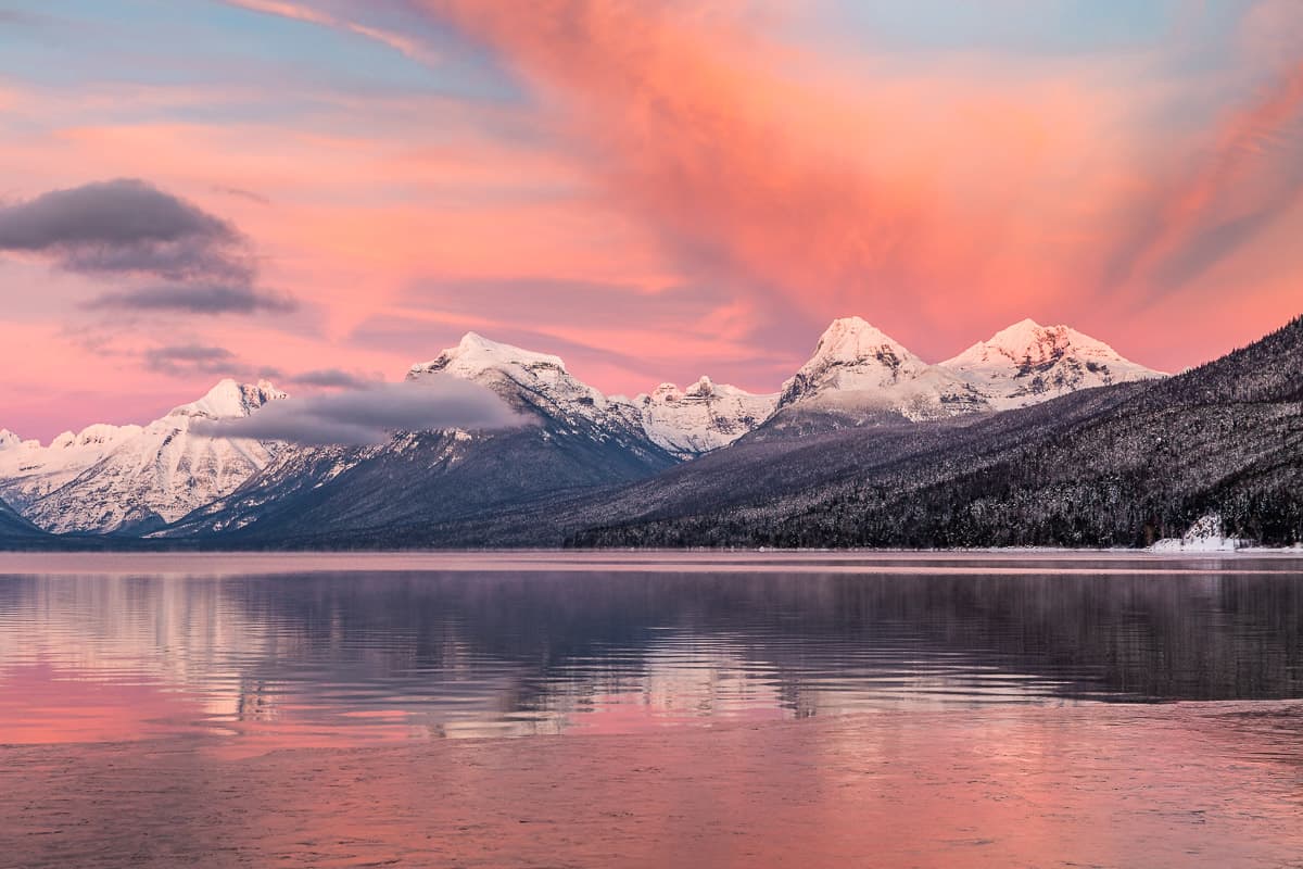 Cotton candy pink sunset over the mountains in Glacier National Park with reflection in the lake.