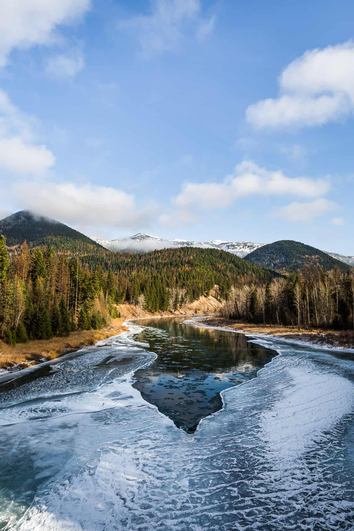 Mostly frozen river with some open water and a mountain backdrop.