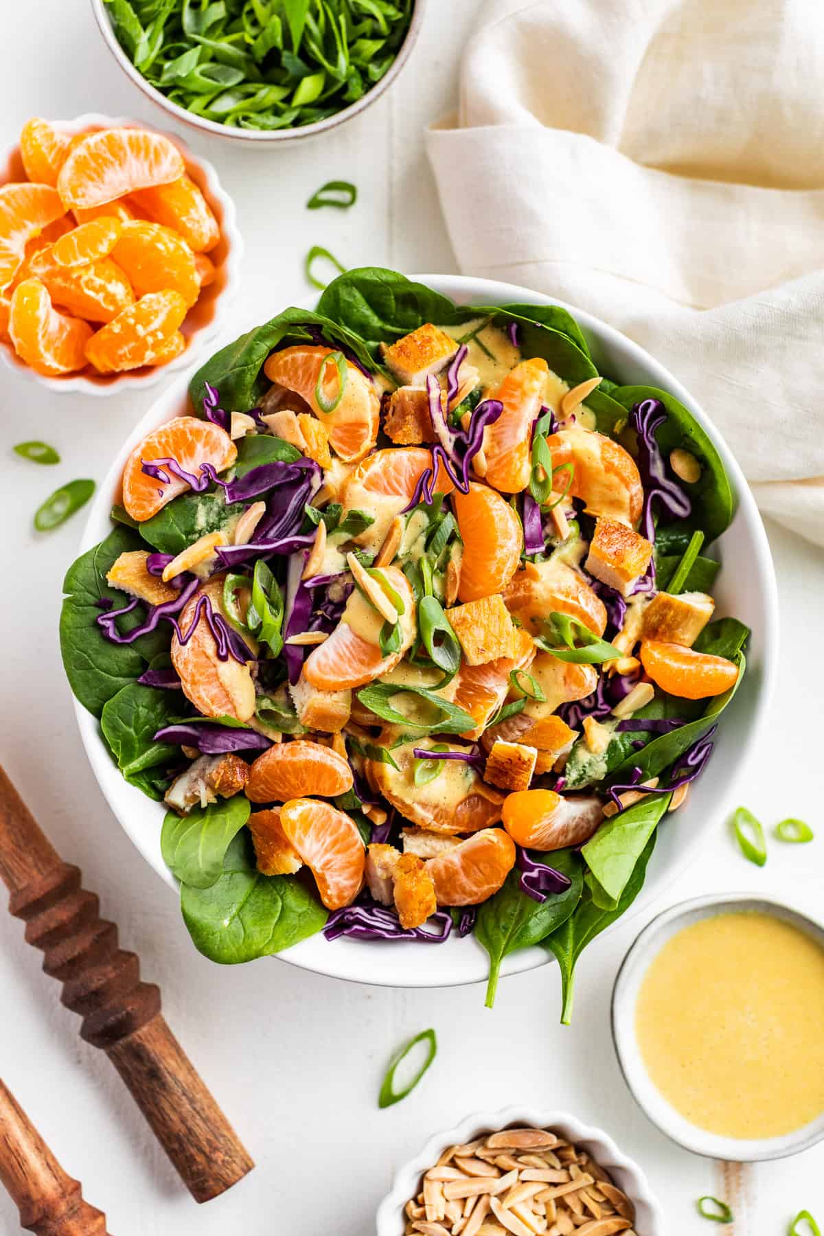 Downward view of Mandarin Chicken Salad in a white bowl with ginger dressing, Mandarin oranges, and green onions on the side.