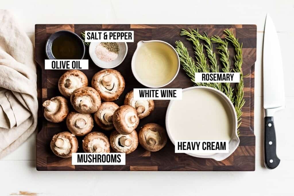 Mushrooms, heavy cream, white wine, and rosemary on a wooden cutting board.