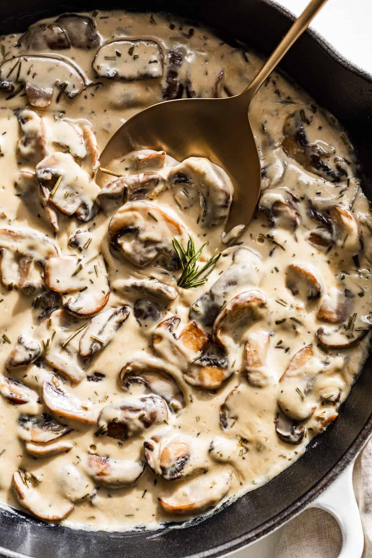 Close view of Mushrooms Cream Sauce with a gold spoon and rosemary.