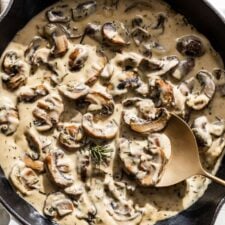 Close view of creamy mushroom sauce with a gold spoon in a white skillet.