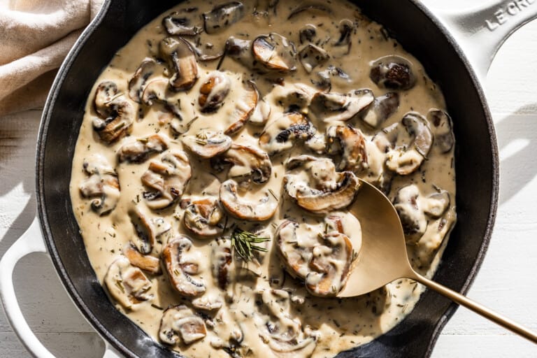 Close view of creamy mushroom sauce with a gold spoon in a white skillet.