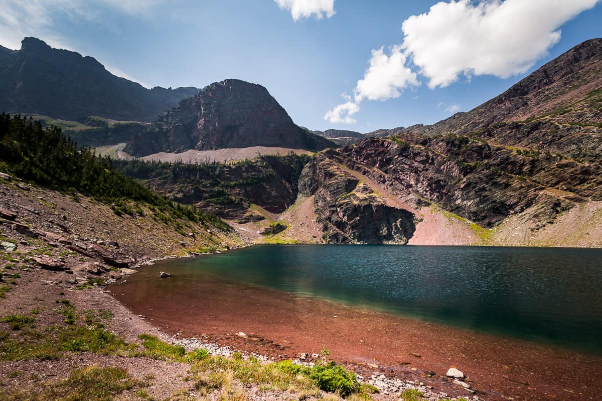 Otokomi Lake in Glacier National Park a deep blue lake with red rock at the bottom and red rock cliffs around it.