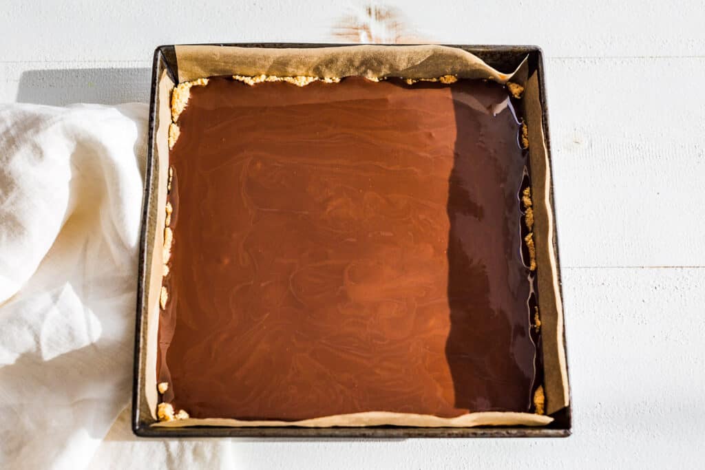 The chocolate layer being added over the top of the chilled caramel layer.