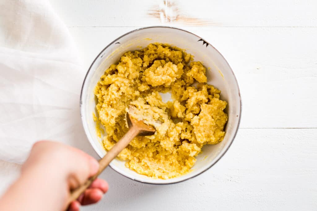 Shortbread crust being mixed together with a wooden spoon in a white bowl.