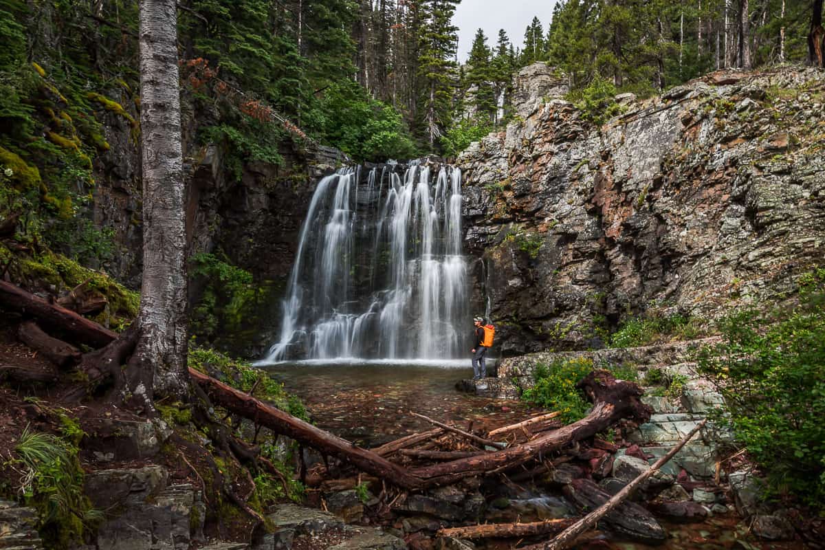 Man with an orange backpack looking at a waterfall.