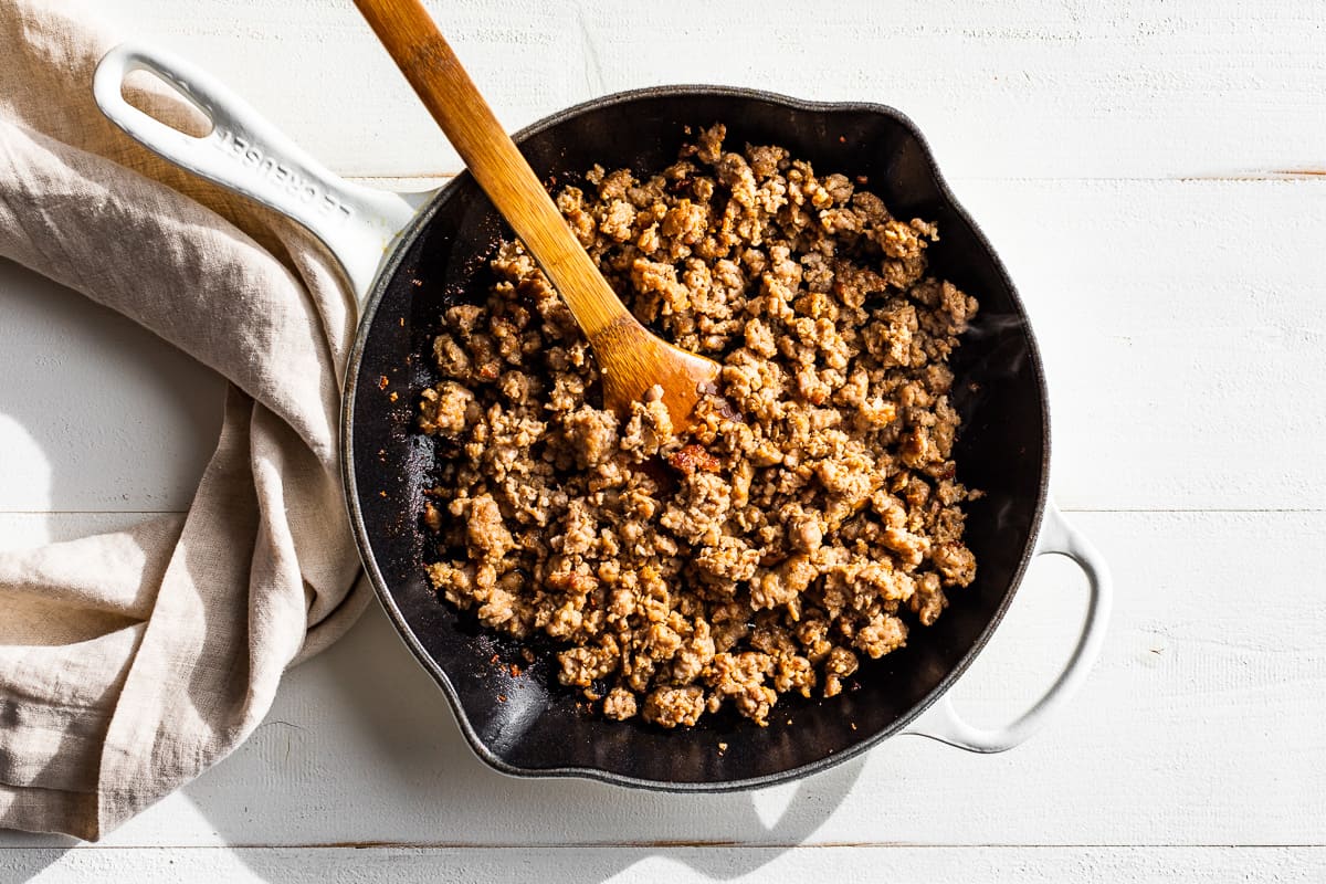 Browned sausage in a white cast iron skillet.