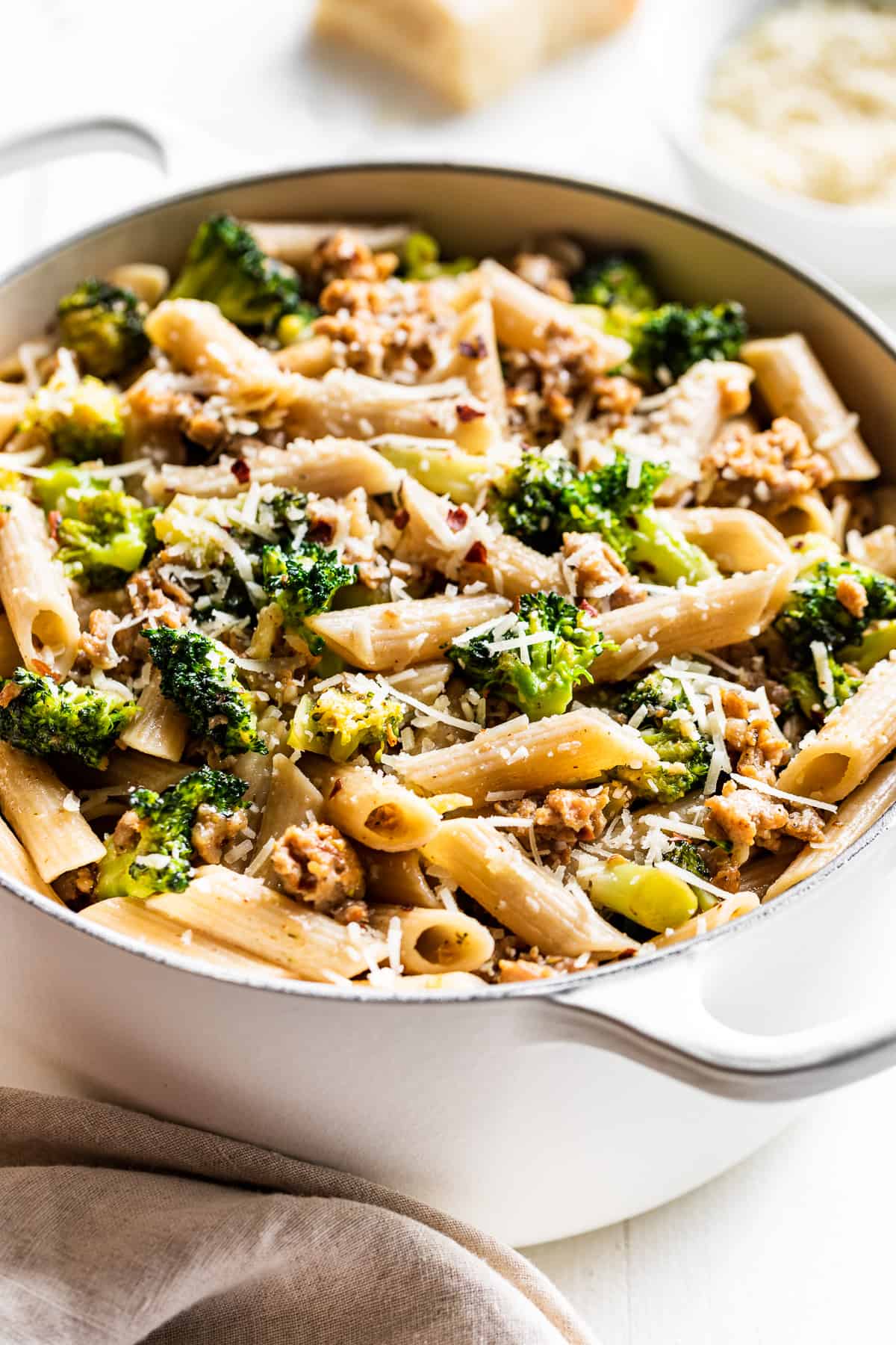 Side view of Sausage Broccoli Pasta in a large white pot with parmesan cheese on the side.