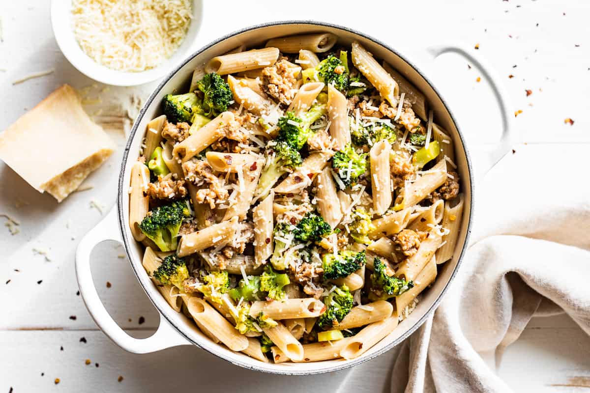 Sausage Broccoli Pasta in a large white pot with grated parmesan cheese on the side.