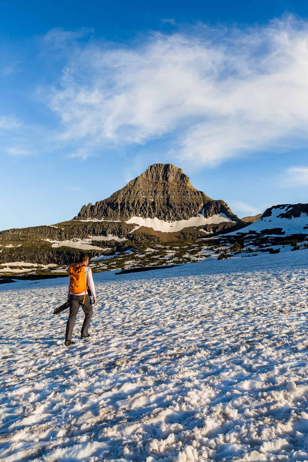 Man crossing a snow field with a mountain peak in the distance.