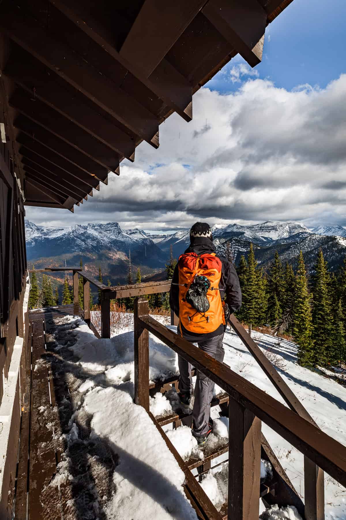 Man standing on a mountain lookout looking at a large snowy mountain in the distance.