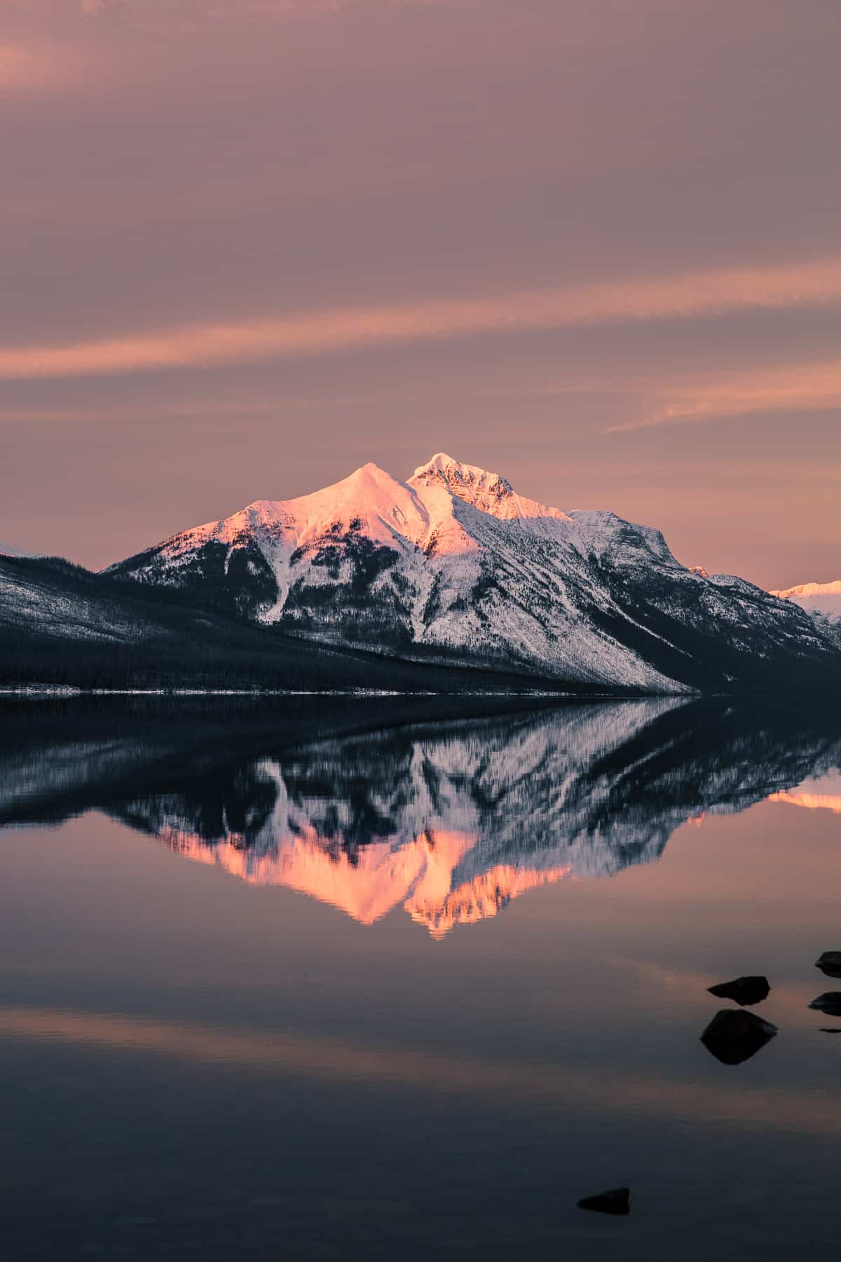 Mountain reflecting into a lake with a light pink sunset glow.