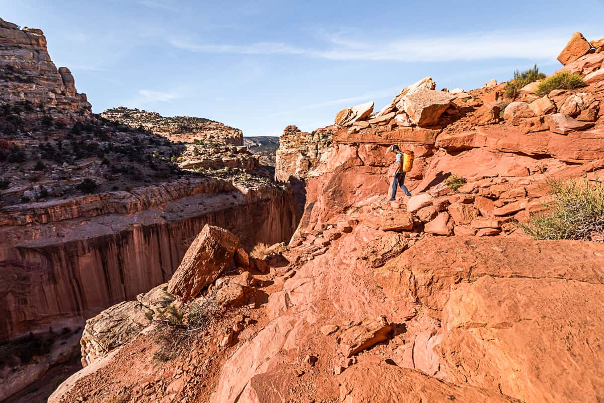 Man hiking down the orange rock trail with blue skies in the background.