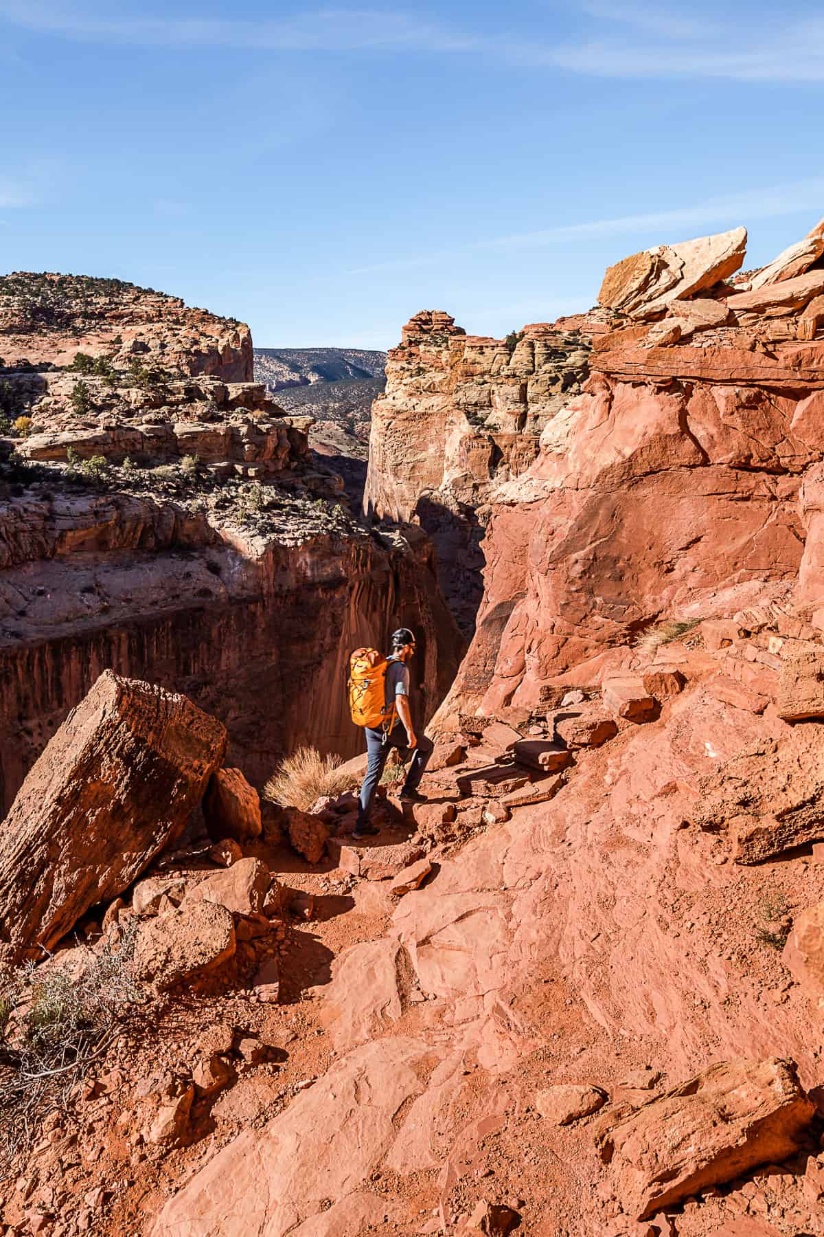 Man with an orange backpack heading up the Cassidy Arch Trail which is made up of orange rock.