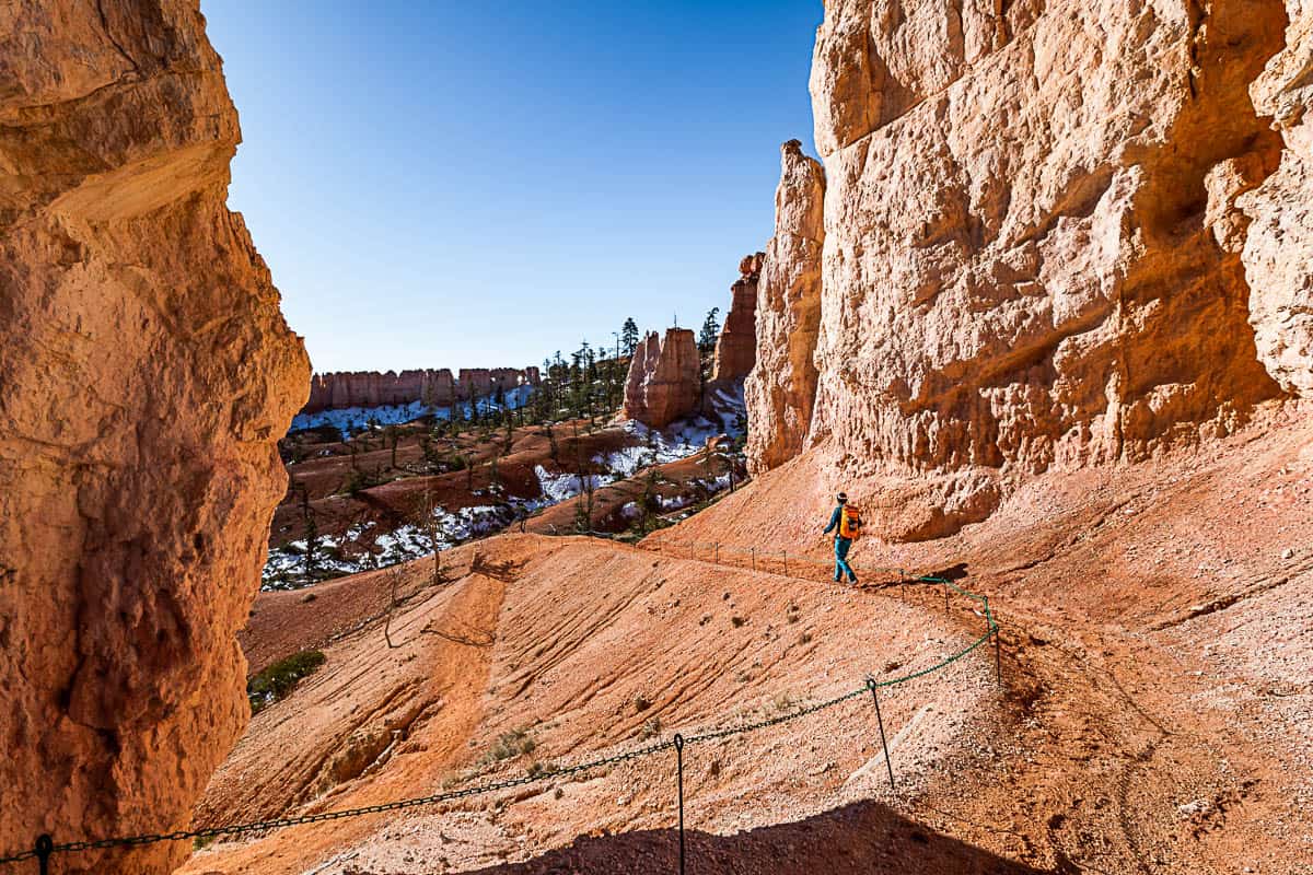 Orange dirt trail with tall hoodoo formations on each side.