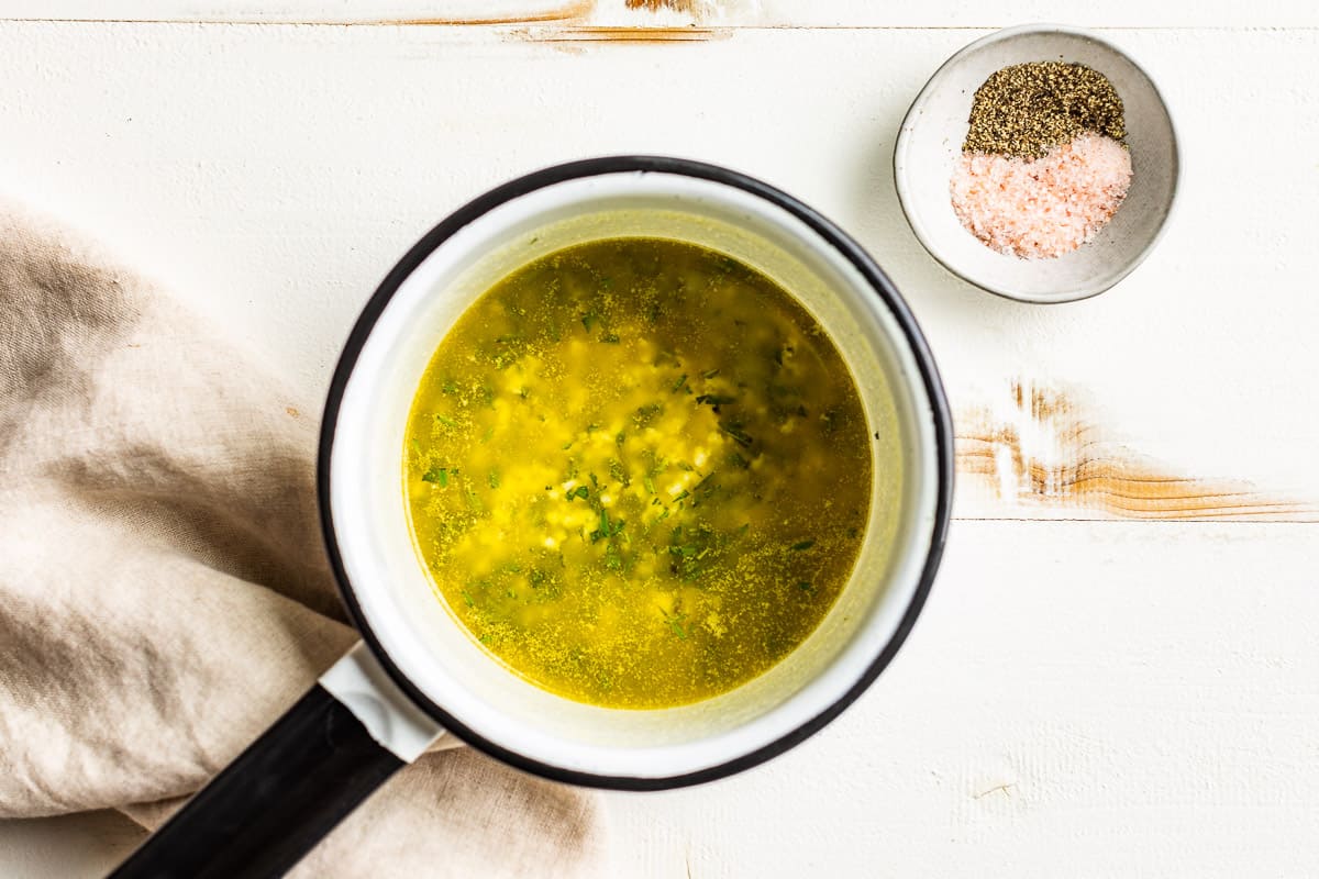 Melted butter in a saucepan with garlic and herbs added.